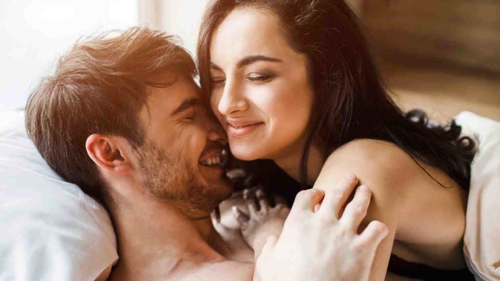 Image of a happy couple in bed, where the man is practicing semen retention.